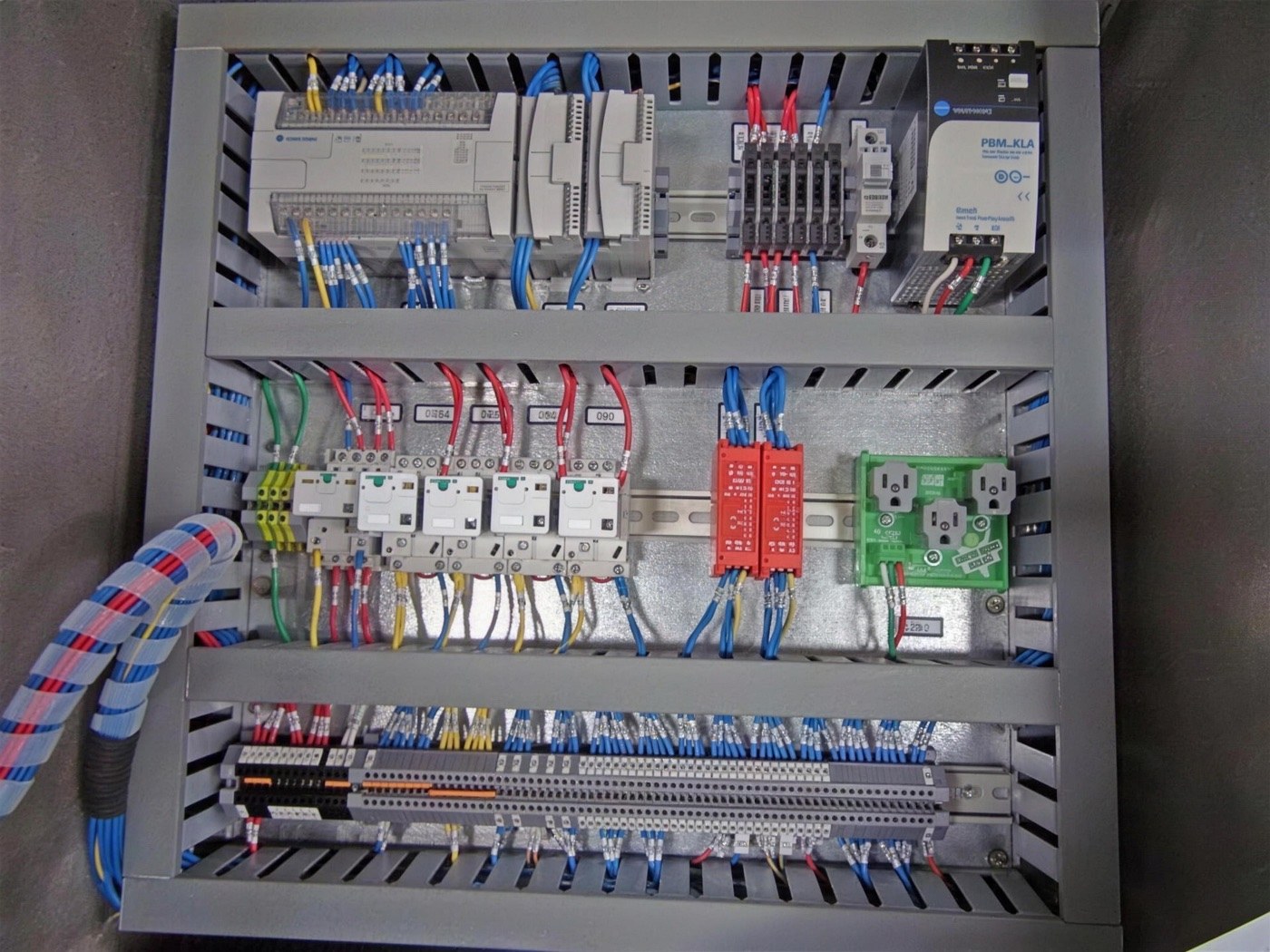 Inside a System Technology control panel: PLC, power supply, safety relays and labeled wiring