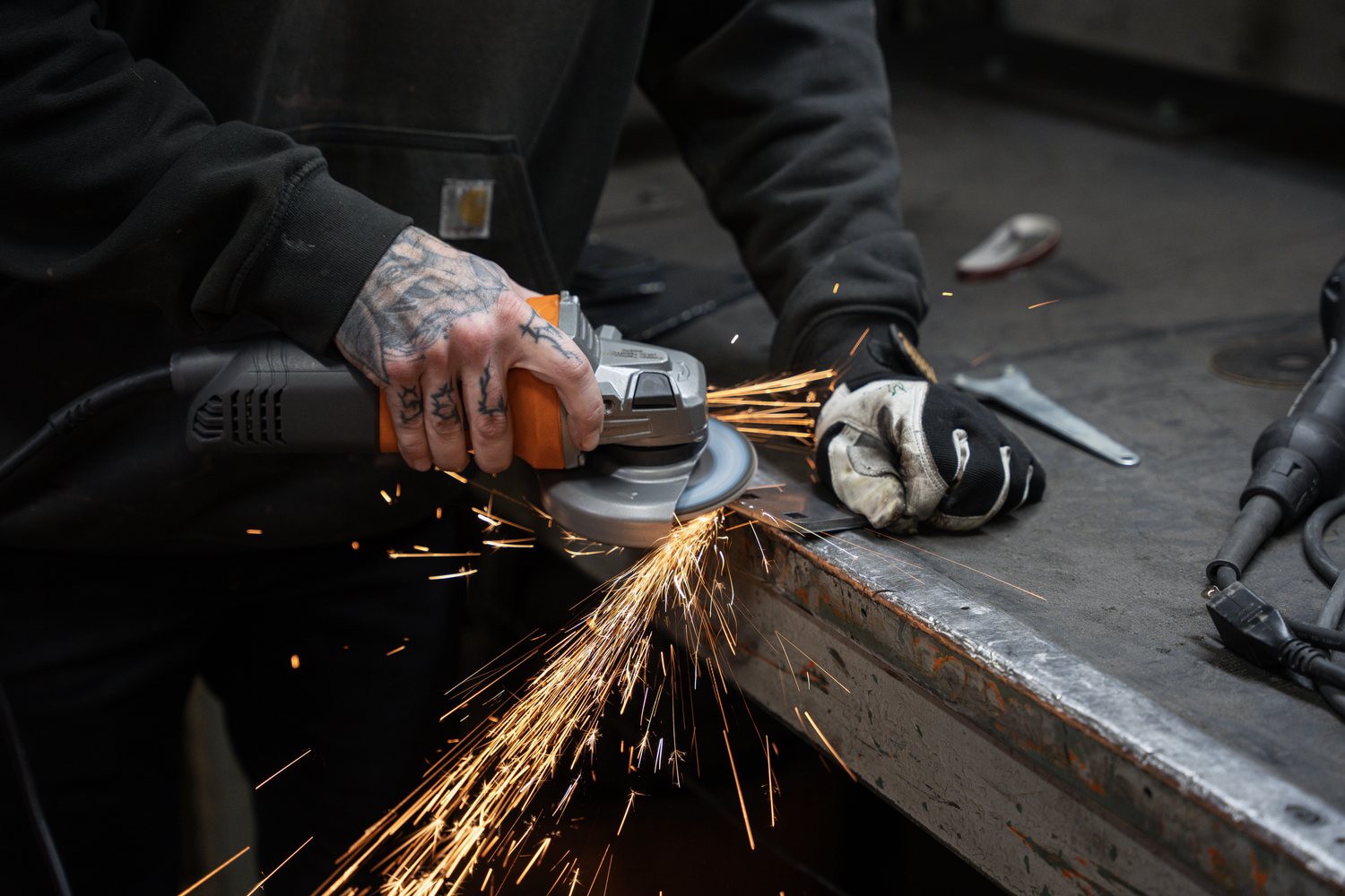A fabricator grinding steel, throwing a spray of sparks