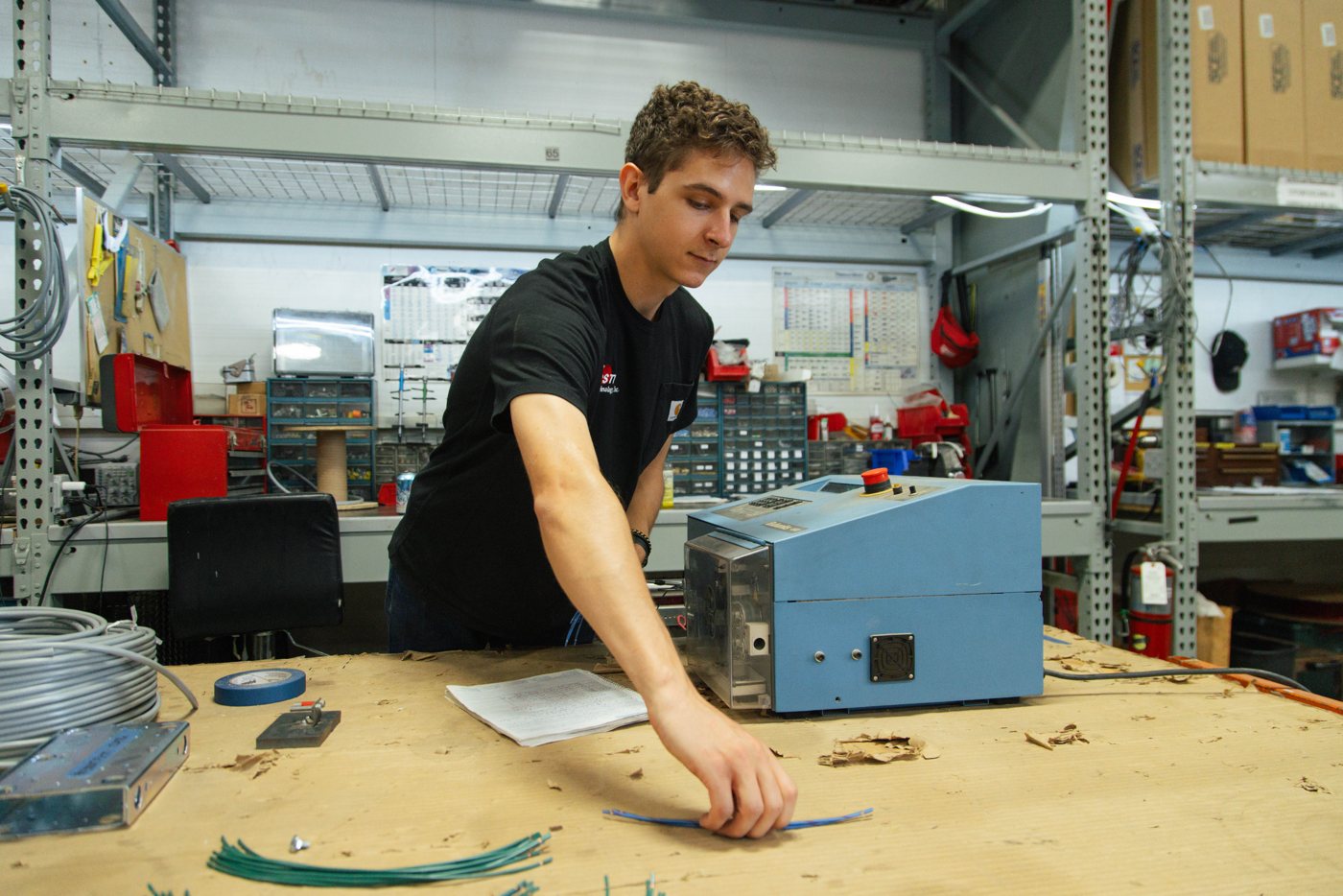 An STI technician wiring a control unit at a bench in the Joliet shop